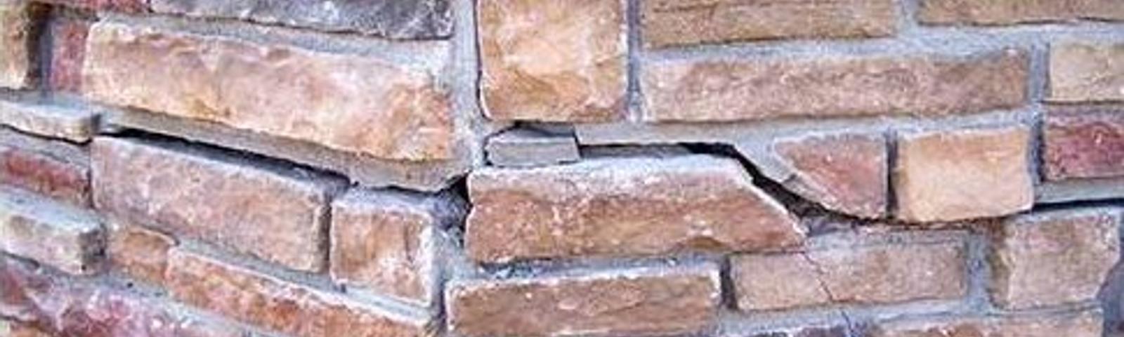 Close-up of a stone wall corner with varied shades of brown and a noticeable crack in one of the stones.
