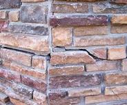 Close-up of a stone wall corner with varied shades of brown and a noticeable crack in one of the stones.