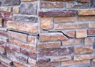 Close-up of a stone wall corner with varied shades of brown and a noticeable crack in one of the stones.