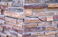 Close-up of a stone wall corner with varied shades of brown and a noticeable crack in one of the stones.