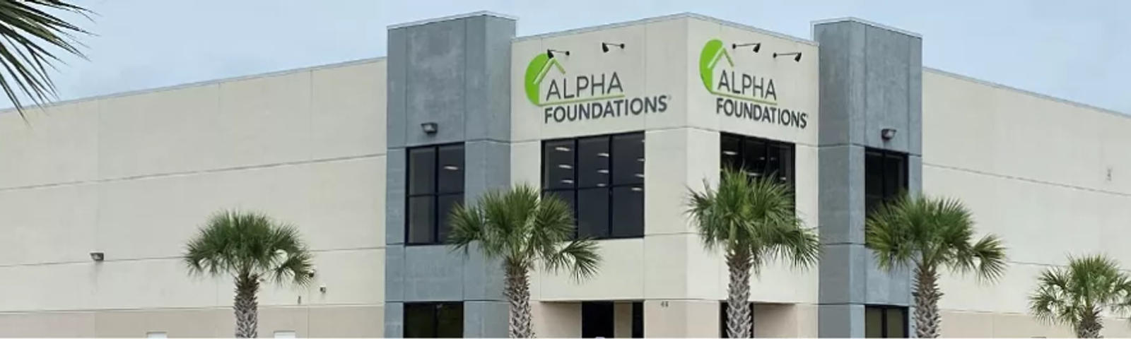 Commercial building with "Alpha Foundations" signage and palm trees in front.