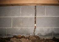 Cracked concrete block foundation with visible gap and soil at the base.