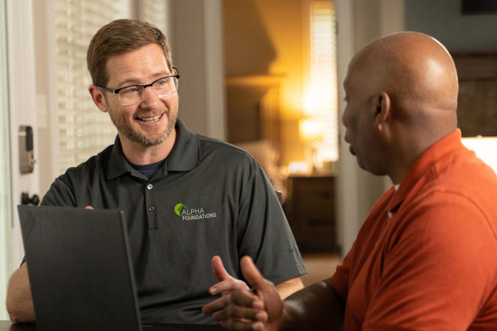 Two men talking at a table, one wearing glasses and a polo shirt with a company logo.
