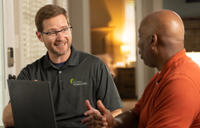 Two men talking at a table, one wearing glasses and a polo shirt with a company logo.