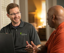 Two men talking at a table, one wearing glasses and a polo shirt with a company logo.