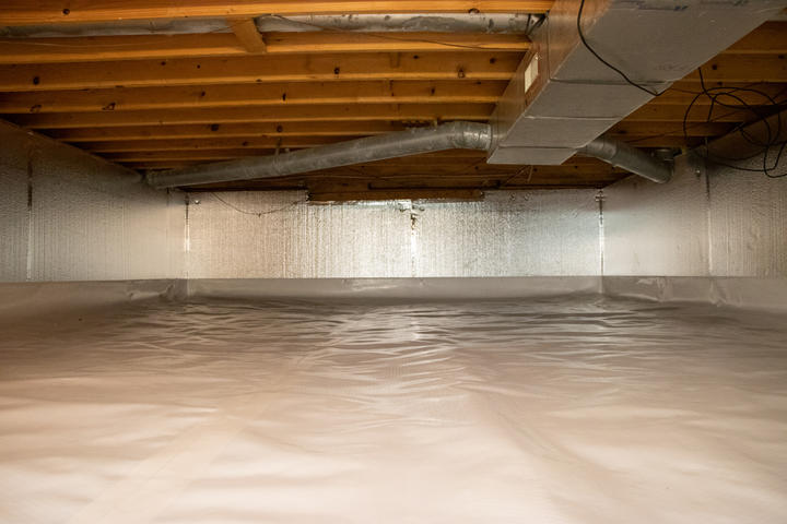 A clean and well-lit crawl space with insulated walls and a plastic-covered floor.