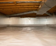 A clean and well-lit crawl space with insulated walls and a plastic-covered floor.