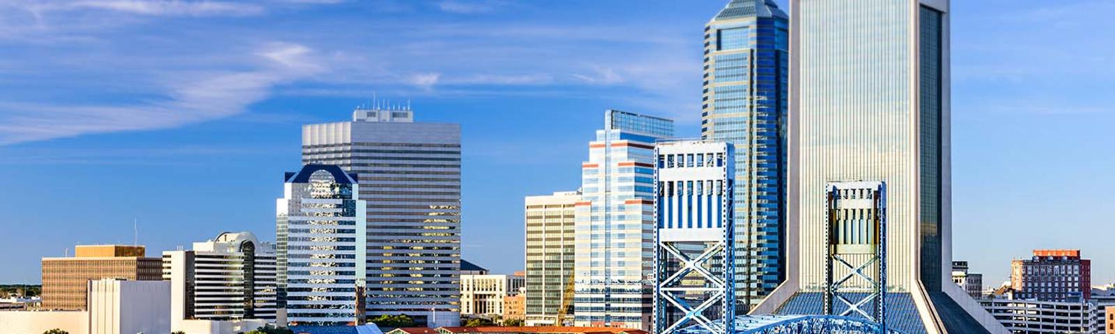 Skyline view of downtown Jacksonville, Florida, with modern skyscrapers and a blue bridge under a clear blue sky.