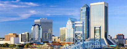 Skyline view of downtown Jacksonville, Florida, with modern skyscrapers and a blue bridge under a clear blue sky.