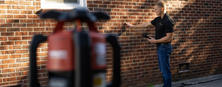 Person using a measuring tool against a brick wall, with equipment in the foreground.