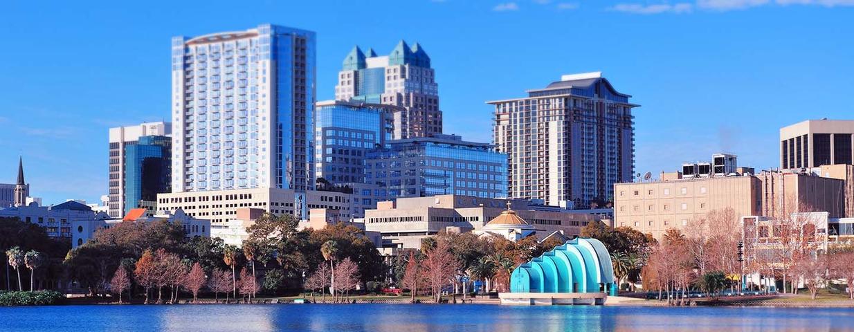 Orlando skyline with tall buildings and a blue structure by a lake under a clear blue sky.