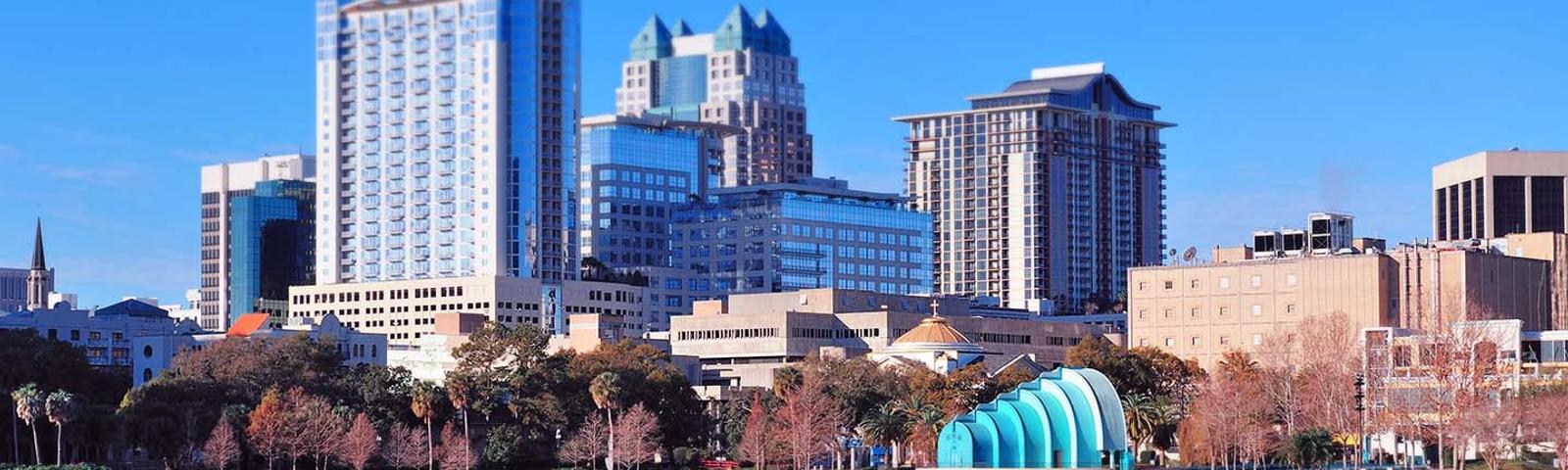 Orlando skyline with tall buildings and a blue structure by a lake under a clear blue sky.