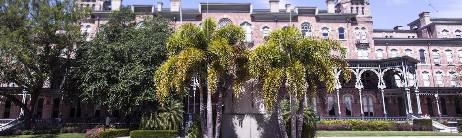 Historic brick building with arched windows, palm trees, and blue sky background.