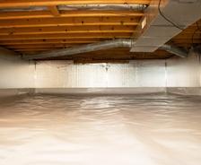 A clean, insulated attic with wooden beams, ducts, and a reflective foil on the walls and ceiling.