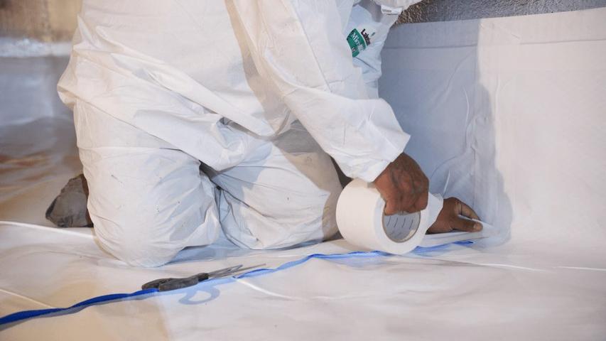Person in protective suit applying white tape on a surface indoors.