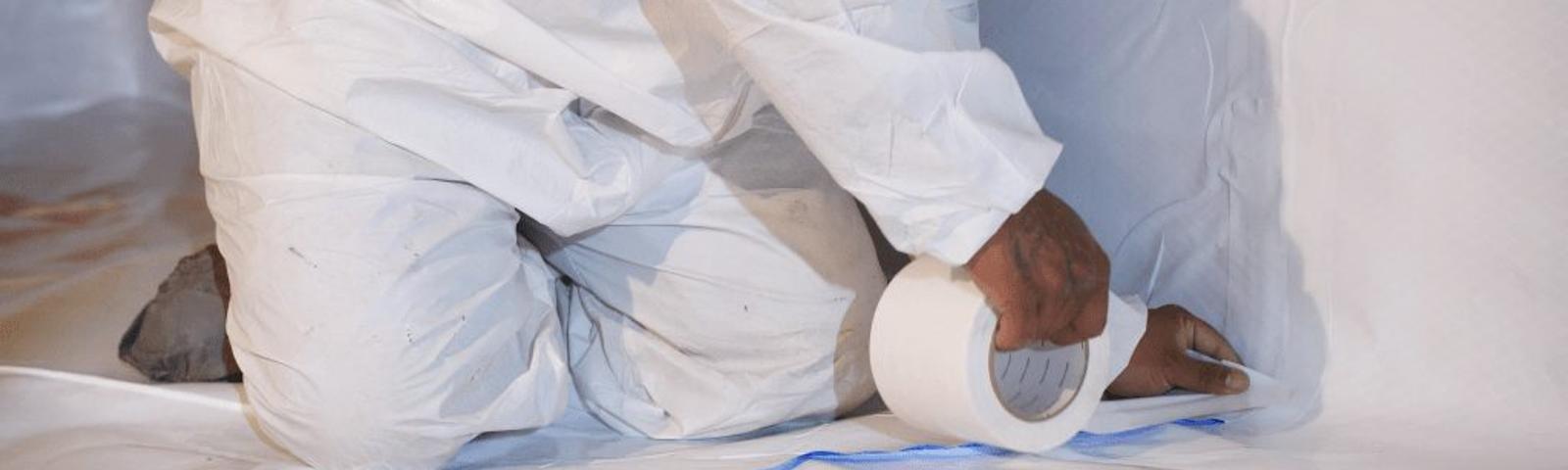 Person in protective suit applying white tape on a surface indoors.