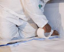 Person in protective suit applying white tape on a surface indoors.