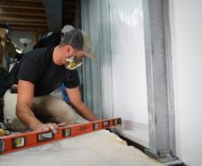 Person using a level tool to align metal framing indoors, wearing a cap and mask.