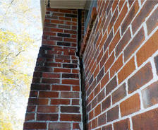 Close-up of a red brick wall with visible gaps and cracks between the bricks.