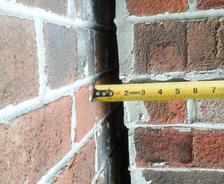 A measuring tape showing a 2-inch gap between two brick walls.