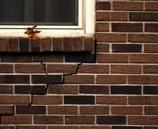 Brick wall with a crack below a window sill where yellow leaves rest.