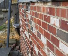 Cracked brick wall with loose mortar next to a wooden staircase shows signs of wear similar to drywall cracks.