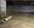 The basement, with standing water, exposed concrete walls, and visible pipes, hints at possible flooding or water damage similar to a flooded crawl space.