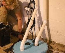 Person installing a sump pump with white pipes in a basement.