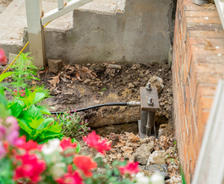 A steel foundation pier installed next to a brick wall and blooming flowers in a garden.