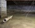 Flooded crawl space under a house with standing water, mud, debris, and exposed pipe.