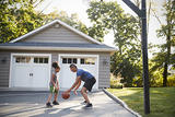 Father and son playing basketball in driveway.