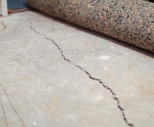 A large crack runs across a concrete floor with carpet padding rolled back.