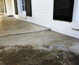 Concrete porch with a noticeable crack and an uneven surface, ready for expert concrete patio repair, near a white brick house with black shutters.