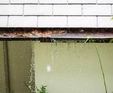 Rainwater overflowing from a roof gutter, causing water to spill down the side of a building—an issue to address in hurricane prep.
