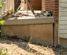 A sinkhole has caused the house foundation to crack, with jacks lifting the porch amid scattered dirt and leaves.