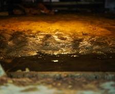 Close-up of a wet, muddy basement floor dimly lit by yellowish light, hinting at rising salinity levels in the area.
