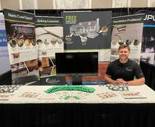 Man sitting at a booth with home improvement displays, brochures, and promotional items on a table.