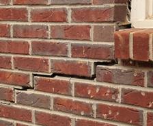 Cracked red brick wall beneath a window hints at possible home foundation issues in Longwood, with bricks shifted out of alignment.