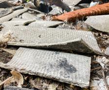 Broken pieces of asbestos cement sheeting and debris scattered on the ground.