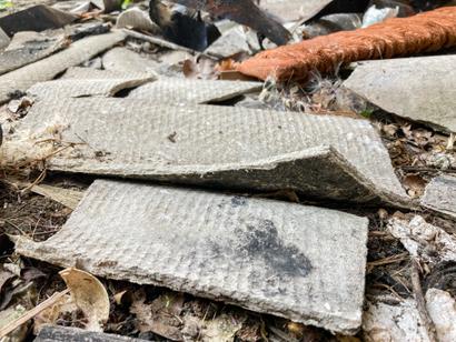 Broken pieces of asbestos cement sheeting and debris scattered on the ground.