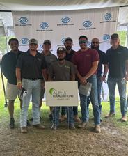 Group of men posing under a tent with an "Alpha Foundations" sign at a Boys & Girls Clubs event.