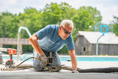 Man wearing gloves and sunglasses busy with pool deck repair, working meticulously on the concrete with equipment.