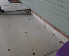 Concrete steps and a landing next to a green-sided house, with scattered leaves and part of a shoe visible.