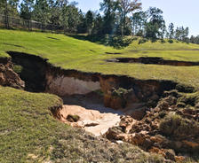 A large sinkhole with eroded ground in a grassy area, showcasing the dangers of sinkholes in Florida.