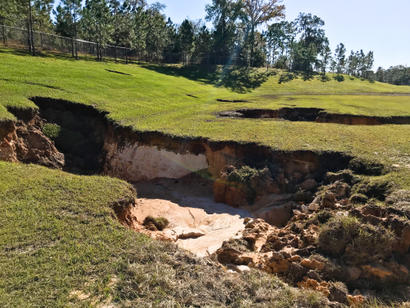 A large sinkhole with eroded ground in a grassy area, showcasing the dangers of sinkholes in Florida.