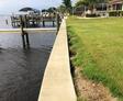 Concrete seawall separates green lawn from waterfront dock on a calm, cloudy day.