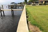 Concrete seawall separates green lawn from waterfront dock on a calm, cloudy day.