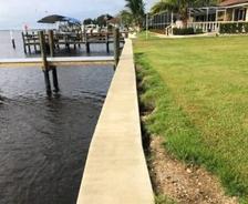 Concrete seawall separates green lawn from waterfront dock on a calm, cloudy day.