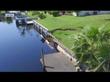 A canal seawall with a large collapsed section and eroded grass, next to a dock and palm tree.