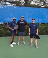 Three Alpha Foundations reps stand on an outdoor pickleball court, holding paddles and smiling at the camera.